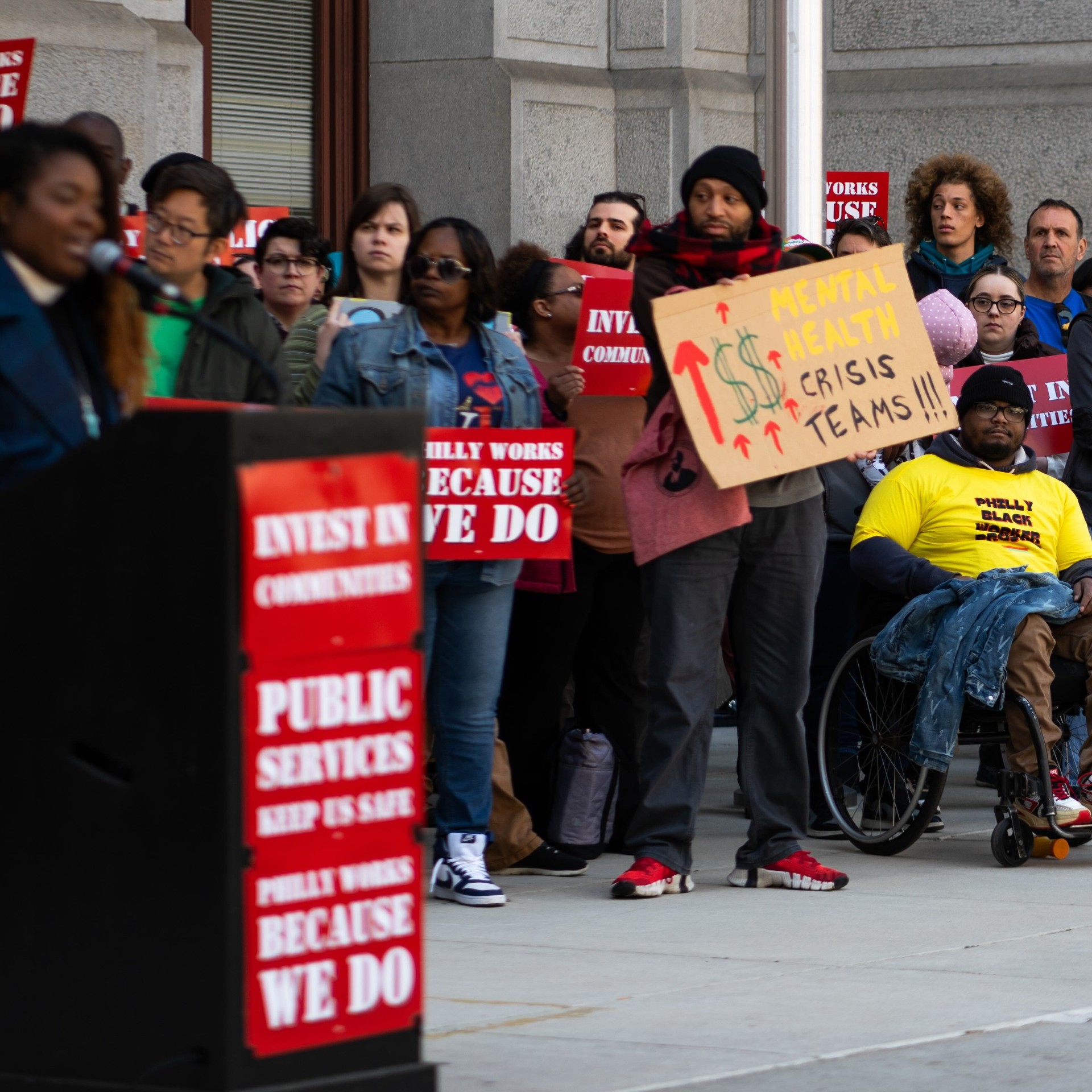 a group gathers for a press conference with signs that read 'more funding for mobile crisis teams'